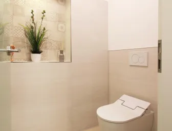 Ein modernes Gäste-WC mit einer wandhängenden Toilette und hellen, beigen Fliesen, die den Raum größer und heller wirken lassen. 