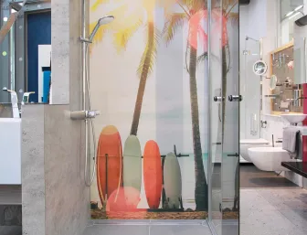 Eine moderne Dusche mit einer großen Glaswand und einer Wandverkleidung, die eine tropische Strandszene mit Palmen und Surfbrettern zeigt.