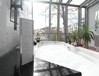 Ein luxuriöser Whirlpool in einem modernen Badezimmer, umgeben von großen Glasfenstern, die viel Tageslicht hereinlassen. 