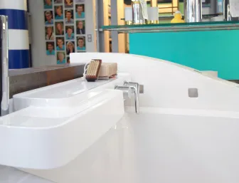 Eine Nahaufnahme einer modernen Badewanne mit einer weißen Ablage, auf der eine Seife und eine Bürste liegen. 