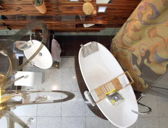 Eine Draufsicht auf eine elegante, freistehende Badewanne mit einem Holztablett, auf dem ein Magazin und ein Weinglas platziert sind. 