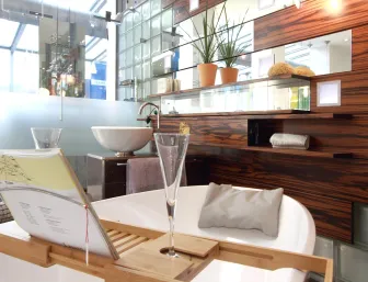 Ein modernes Badezimmer mit einer freistehenden Badewanne, die mit einem Holztablett ausgestattet ist, auf dem ein Buchhalter und ein Champagnerglas stehen.