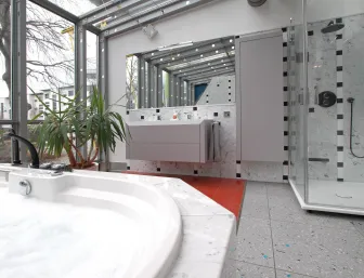 Ein modernes Badezimmer mit einem Whirlpool im Vordergrund, der von großen Fenstern umgeben ist und natürliches Licht hereinlässt. 