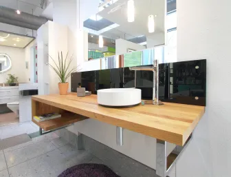 Ein modernes Badezimmer mit einem hölzernen Waschtisch, auf dem ein rundes, weißes Aufsatzwaschbecken und ein verchromter Wasserhahn platziert sind.