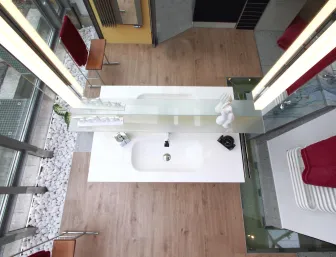 Ein modernes Badezimmer aus der Vogelperspektive zeigt ein elegantes Waschbecken mit einer großen Glasablage, auf der weiße Skulpturen und Accessoires arrangiert sind. 
