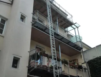 Mehrstöckiges Wohnhaus mit Balkonen, an denen ein Bauaufzug angebracht ist, um Materialien in die oberen Etagen zu transportieren.