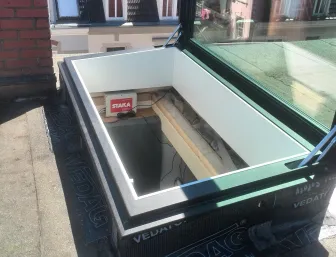 Dachausstieg mit geöffnetem Glasdachfenster, umgeben von Abdichtungsmaterial, mit Blick auf umliegende Häuser und ihre Dachkonstruktionen.
