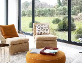 Eleganter Wintergarten mit bodentiefen Fenstern, gemütlicher Sitzgruppe und stilvollen orangefarbenen Akzenten, mit Blick auf einen gepflegten Garten.