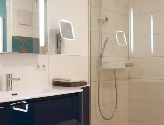 Modernes Badezimmer mit wandhängendem Waschtisch in glänzendem Blau, beleuchtetem Spiegel und einer bodengleichen Dusche mit praktischer Ablage.