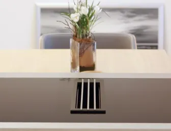 Detailansicht einer modernen Küche mit integriertem Kochfeld und Dunstabzug, dekoriert mit einer stilvollen Vase auf dem angrenzenden Esstisch.