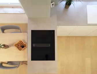 Detailansicht einer modernen Wohnküche mit Kochfeld auf der Insel, integrierter Spüle und einem angrenzenden Essbereich aus hellem Holz.