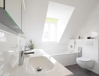 Modernes Badezimmer mit Doppelwaschbecken, wandhängendem WC und Badewanne unter einer Dachschräge.