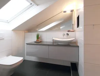 Modernes Badezimmer im Dachgeschoss mit weiß gefliesten Wänden, einem wandhängenden WC und einem stilvollen Waschtisch mit Aufsatzwaschbecken, beleuchtet durch ein großes Dachfenster.