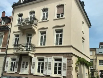 Mehrstöckiges Wohnhaus im klassischen Stil mit dekorativen Balkonen und Fensterläden, an einer ruhigen Straße gelegen.