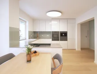 Eine moderne Küche mit glänzend weißen Schränken und einer Arbeitsplatte aus grauem Stein, die sich harmonisch ins Gesamtbild einfügt.