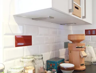 Eine detailreiche Küchenzeile mit glänzenden, weißen Metrofliesen, die durch einzelne rote Akzente aufgelockert wird.