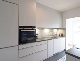 Eine moderne Einbauküche mit weißen, grifflosen Schränken und einer dunklen Arbeitsplatte, die sich entlang einer Wand erstreckt. 