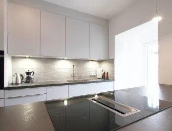 Eine moderne Küche mit grauen Schränken und einer dunklen Arbeitsplatte, die durch eine Rückwand aus glänzenden Metrofliesen ergänzt wird. 