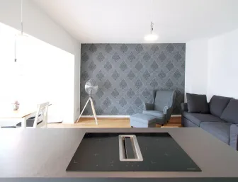 Ein modernes Wohnzimmer mit einer eleganten grauen Tapetenwand, die ein filigranes Muster aufweist. 