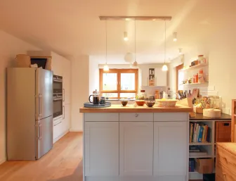 Eine geräumige Wohnküche mit einer zentralen Kücheninsel, die eine Holzarbeitsplatte und offene Regalfächer bietet.