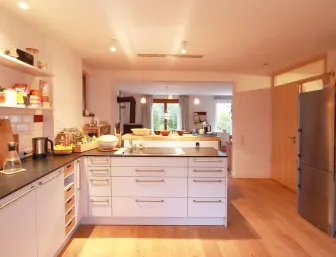 Eine offene Wohnküche mit einer zentralen Kücheninsel, weißen Schränken und dunklen Arbeitsplatten. 