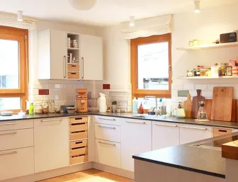 Eine helle, moderne Küche mit weißen Schränken und einer dunklen Arbeitsplatte, die U-förmig angeordnet ist.