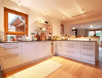 Eine moderne, helle Küche mit weißen Schränken und einer dunklen Arbeitsplatte, die in U-Form angeordnet ist.