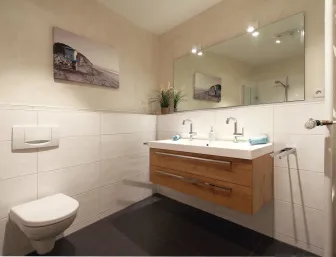 Ein modernes Badezimmer mit einer wandhängenden Toilette und einem eleganten Doppelwaschbecken mit Holzunterschrank.