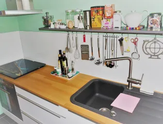 Eine kompakte Küche mit einer hellen Holzarbeitsplatte und einem schwarzen Spülbecken mit moderner Edelstahlarmatur. 