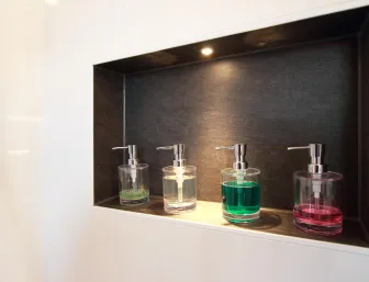 Ein eingebautes Wandregal mit dunklem Hintergrund, das von einer kleinen Lampe oben beleuchtet wird. 