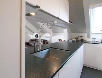 Eine moderne Dachgeschossküche mit einer schwarzen Arbeitsplatte und einem eingelassenen Edelstahlspülbecken.