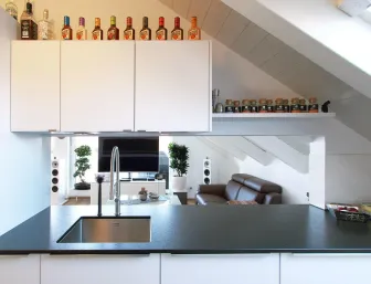 Eine stilvolle Küche unter einer Dachschräge mit einer dunklen Arbeitsplatte und einem eingebauten Edelstahlspülbecken.