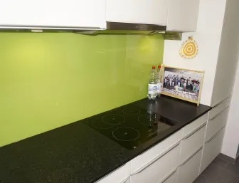 Eine kompakte Küche mit weißen, grifflosen Schränken und einer schwarzen Granitarbeitsplatte, die sich durch eine glänzend grüne Glasrückwand abhebt. 