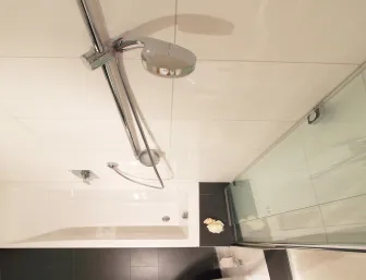 Eine moderne Badezimmeransicht mit einer rechteckigen weißen Badewanne, die mit einer Glasduschabtrennung kombiniert ist. 