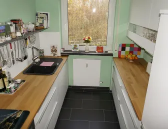 Eine kleine Küche mit weißen Schränken und Arbeitsplatten aus hellem Holz, kombiniert mit einem schwarzen Spülbecken und Edelstahlarmatur.