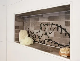Eine in die Wand integrierte Ablage im Badezimmer mit braunen Fliesen, die eine Zeichnung eines Katzenmotivs als dekoratives Element enthalten. 