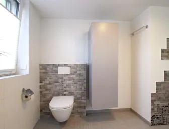 Ein Badezimmer mit einer modernen Wandtoilette, die in eine Wand mit braunen Mosaikfliesen integriert ist.