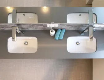 Ein Doppelwaschtisch mit zwei rechteckigen, weißen Waschbecken und modernen Wasserhähnen aus Edelstahl, von oben fotografiert.