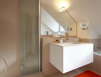 Ein modernes Badezimmer unter einer Dachschräge mit einer gläsernen Dusche auf der linken Seite und einer weißen Badewanne auf der rechten.
