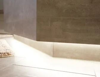 Detailaufnahme eines wandhängenden Badschranks in moderner Betonoptik mit indirekter Bodenbeleuchtung. Die Lichtakzente betonen die Fliesen und den Teppich im Badezimmer.