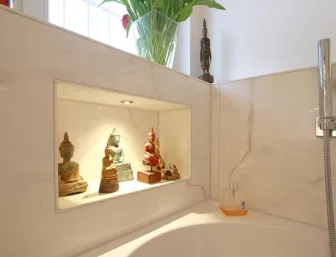 Detailaufnahme einer beleuchteten Wandnische im Badezimmer mit kleinen Buddha-Statuen und Dekorationsobjekten, umgeben von eleganter Marmorgestaltung.