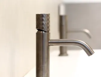 Detailaufnahme einer Edelstahl-Waschtischarmatur auf weißem Becken in der Badausstellung von Lassen.