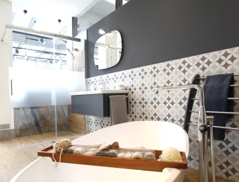Freistehende Badewanne mit Designfliesen, Handtuchheizkörper und Pendelleuchte in der Badausstellung von Lassen.