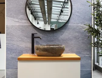 Naturstein-Aufsatzwaschbecken mit rundem Spiegel und schwarzer Armatur in der Badausstellung von Lassen.