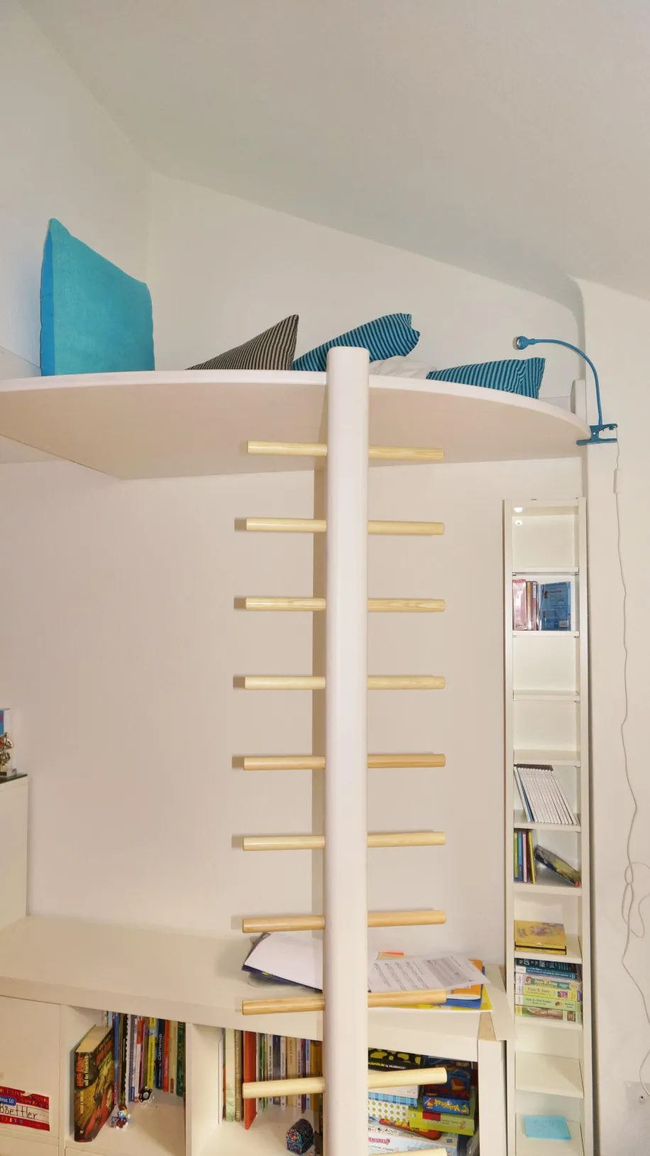 Ein Kinderzimmer mit einer Hochbettkonstruktion, die über eine vertikale Leiter mit Holzsprossen erreichbar ist. 