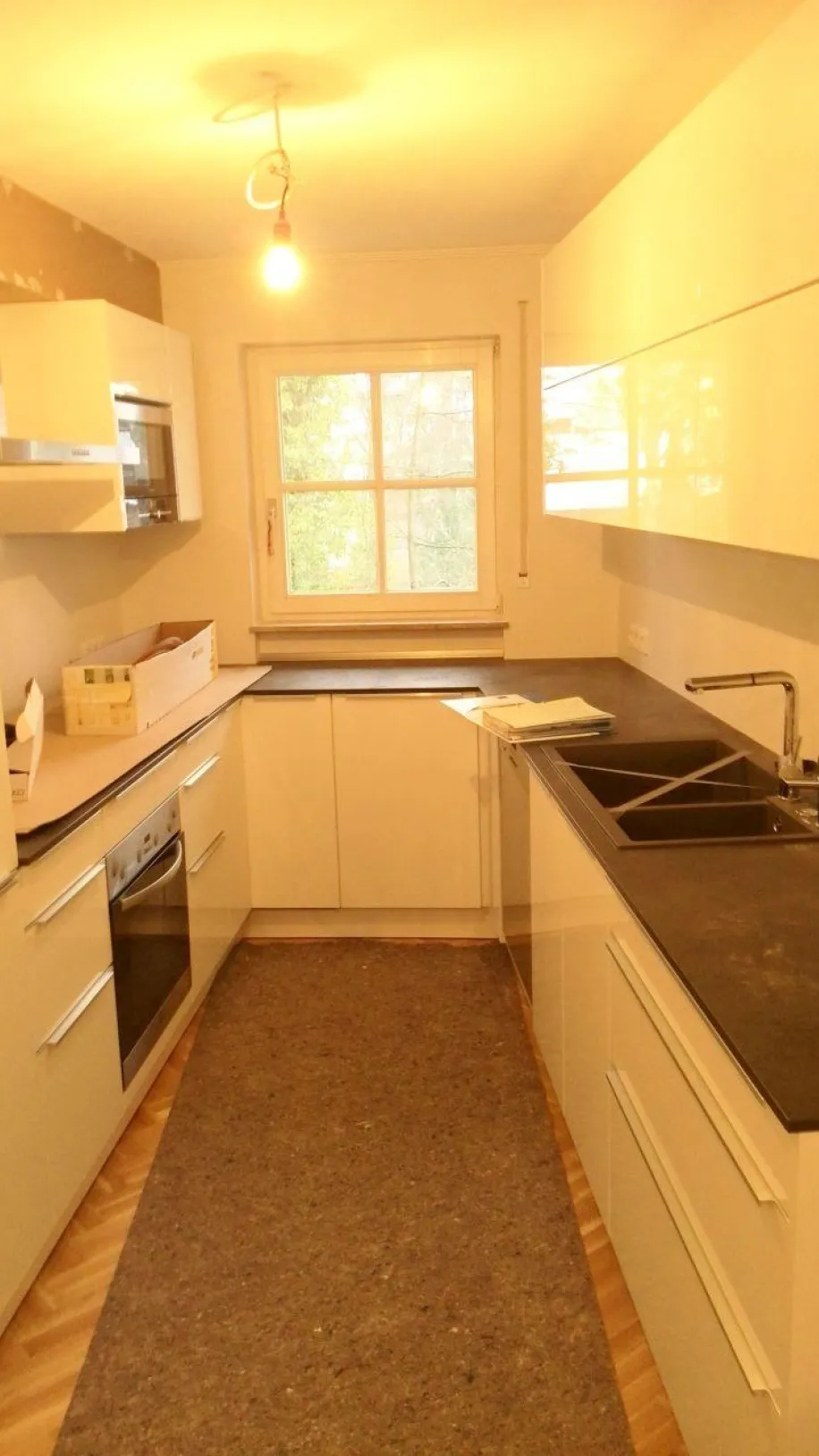 Eine moderne Einbauküche mit glänzend weißen Fronten und dunklen Arbeitsplatten, die in einem kompakten, schlauchförmigen Layout gestaltet ist. 