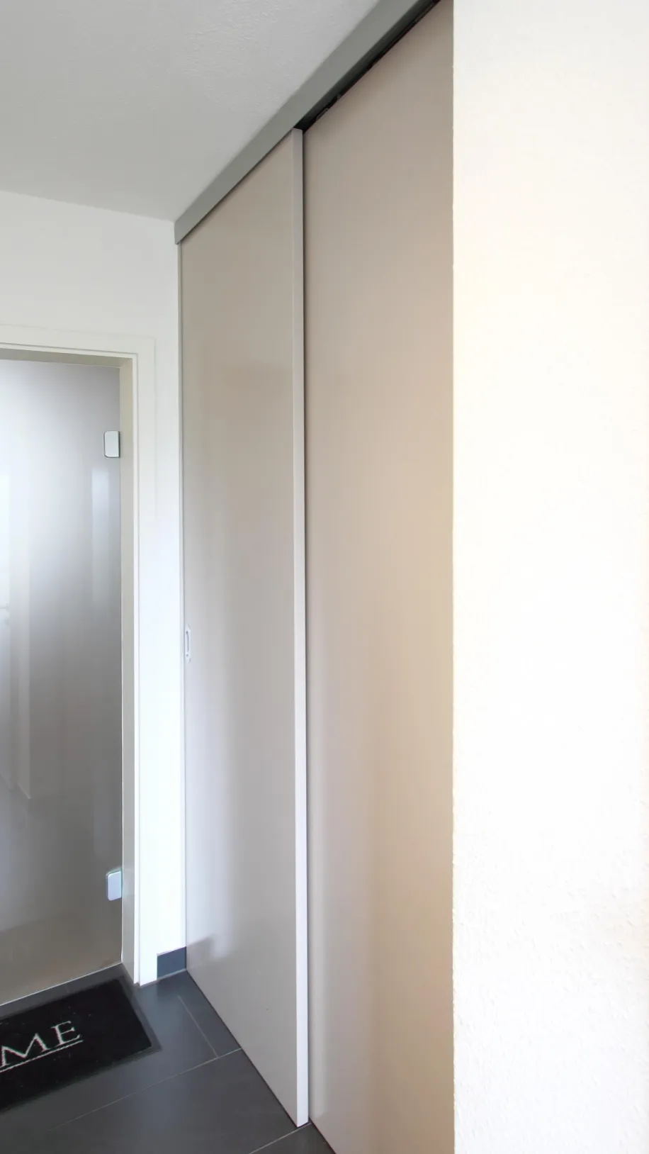 Ein moderner Flur mit einer eleganten, beigefarbenen Schiebetür, die bündig in die Wand integriert ist.