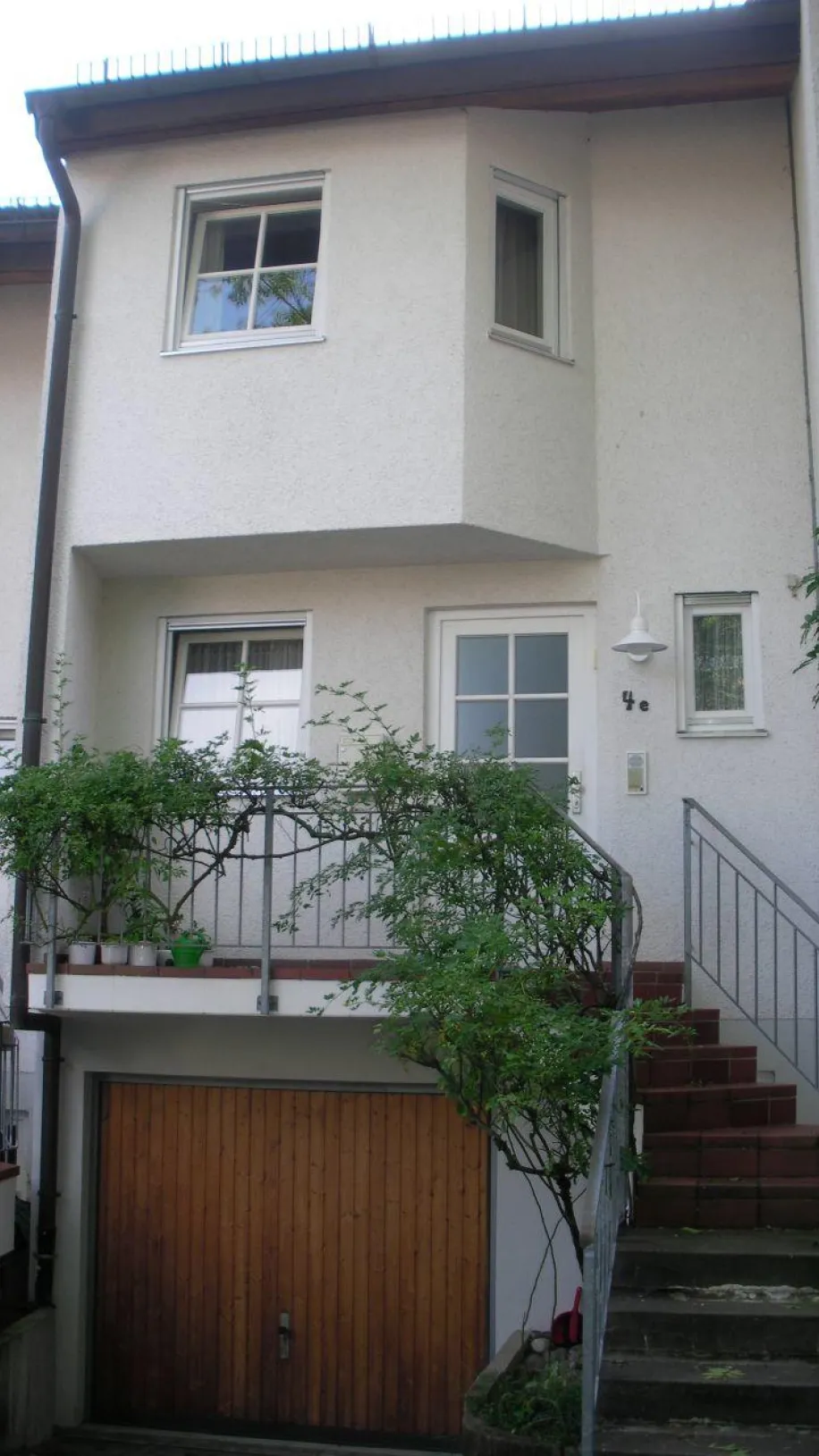 Ein dreistöckiges Reihenhaus mit einer weißen Fassade und einem kleinen Balkon, der von einem Geländer mit Kletterpflanzen umgeben ist.