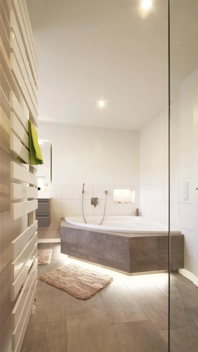 Modernes Badezimmer mit großer Eckbadewanne, beleuchteter Verkleidung und Handtuchheizkörper, in harmonischen Erdtönen gestaltet für eine entspannte Atmosphäre.