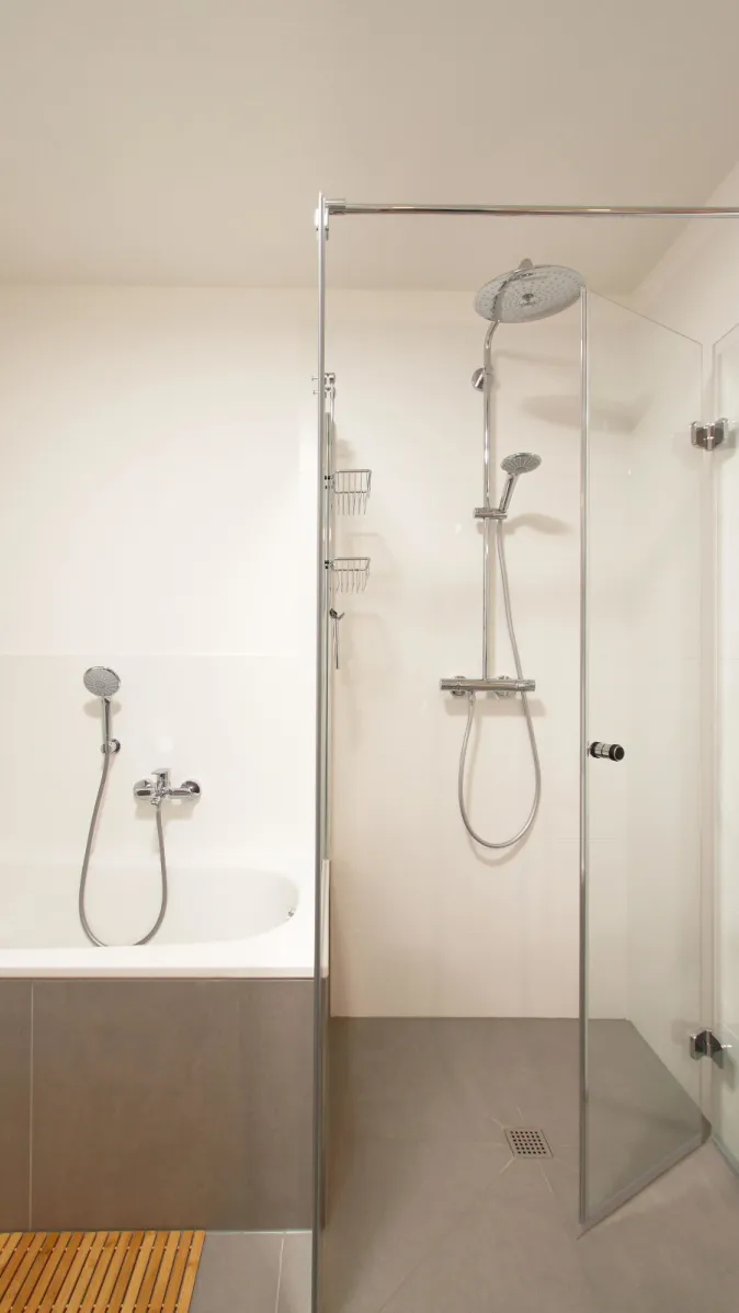 Modernes Badezimmer mit freistehender Dusche und Badewanne. Glasabtrennung und schlichte Armaturen sorgen für ein minimalistisches und zeitloses Design.